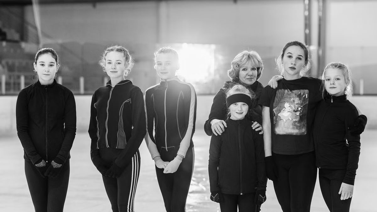 A group of female ice skaters pose together indoors. Black and white photograph.